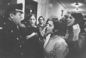 Black and white image of women being blocked from entering a room by a police officer